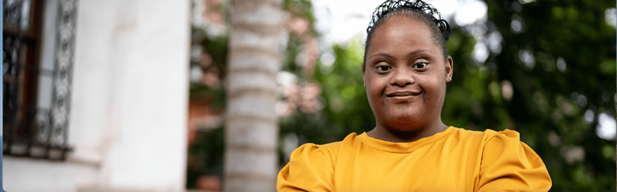Young girl with Down syndrome in a yellow top, smiling.